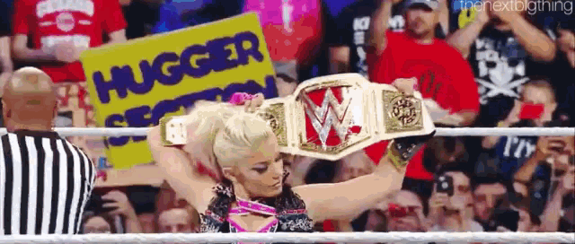 a woman is holding a wrestling championship belt in front of a crowd with a sign that says hugged section