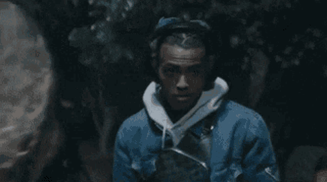 a man wearing headphones and a blue denim jacket is standing in the dark .