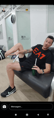 a man wearing a black ea7 shirt sits on a couch with his legs crossed