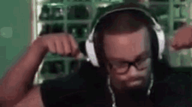 a man wearing headphones and glasses is flexing his muscles in a video call .
