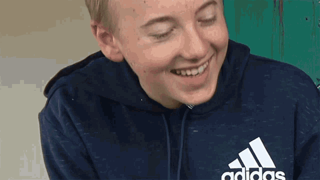 a boy wearing a blue adidas sweatshirt smiles