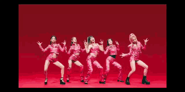 a group of women in pink outfits are standing next to each other and dancing on a red background .