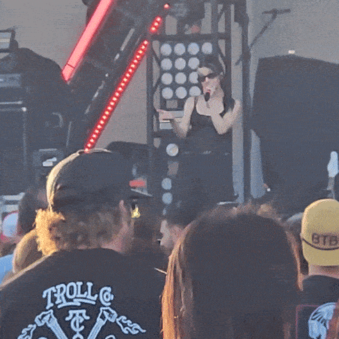 a woman singing into a microphone in front of a crowd with a yellow hat that says stb on it