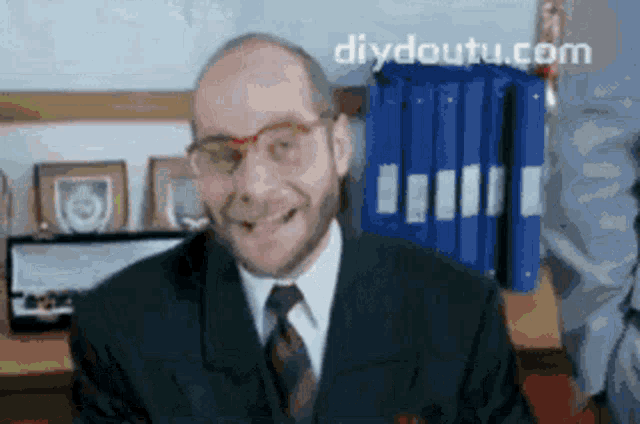 a man wearing glasses and a suit is smiling in front of a diydoutu.com logo