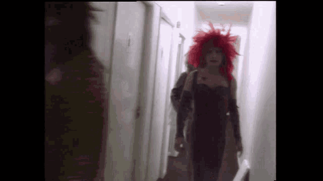 a woman with red hair and a black dress is walking down a hallway