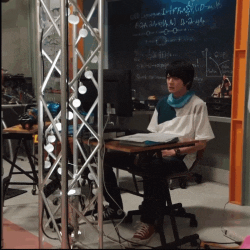 a man sits at a desk in front of a chalkboard that says ' g ' on it