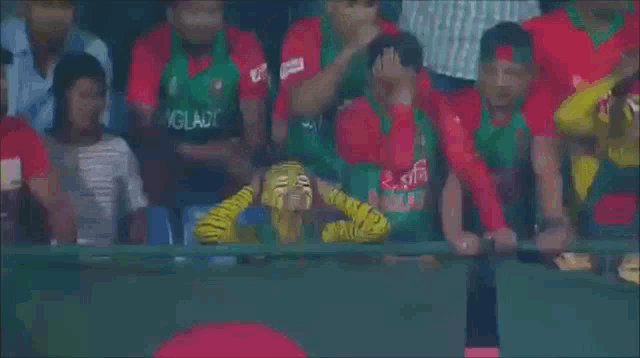 a man wearing a green shirt that says bangladesh is sitting in a crowd of people
