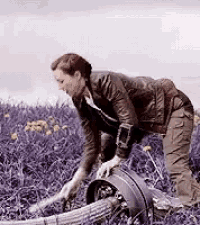 a man is kneeling down in a field of purple flowers holding a bucket .