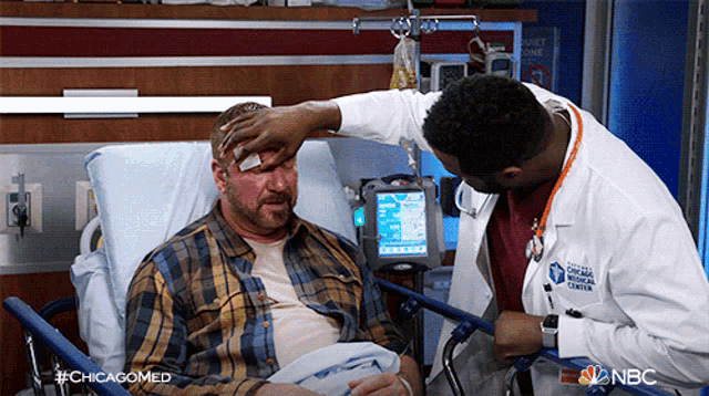 a man in a hospital bed is talking to a doctor who is wearing a chicago medical center shirt