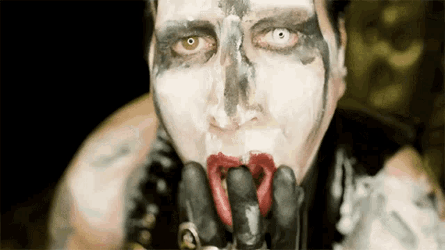 a man with white paint on his face is licking his fingers