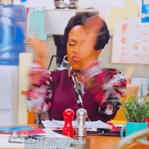 a woman sitting at a desk with a sign that says it 's to go help hazel in your class ..