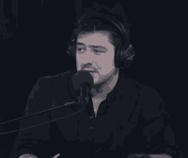 a man wearing headphones and a black shirt is speaking into a microphone