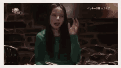 a woman with long black hair is sitting at a table with her hands up .