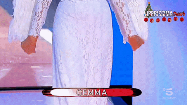 a woman in a white dress is standing in front of a screen with the name gemma on it