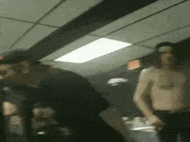 a shirtless man is standing next to another shirtless man in a dark room