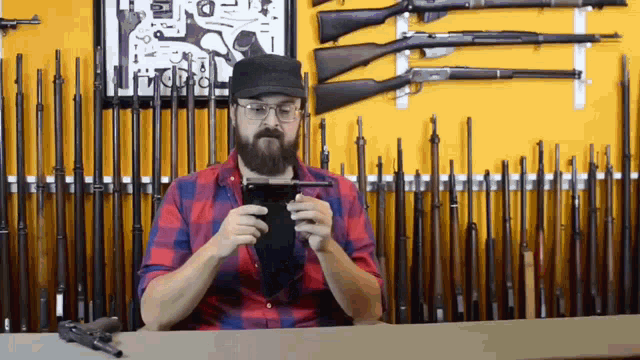 a man with a beard and glasses is using a tablet in front of a wall of guns