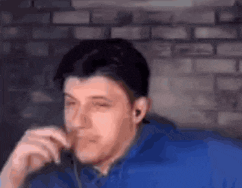 a man in a blue shirt is sitting in front of a brick wall .