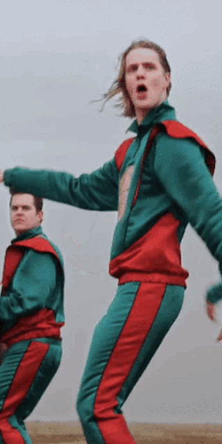 a man in a green and red tracksuit stands next to another man