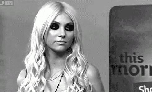 a black and white photo of a woman with long blonde hair standing in front of a sign that says this more .