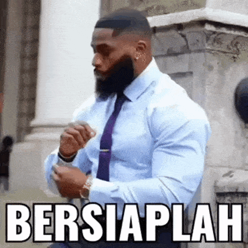 a man in a blue shirt and purple tie is standing in front of a building with the words bersiaplah written above him .