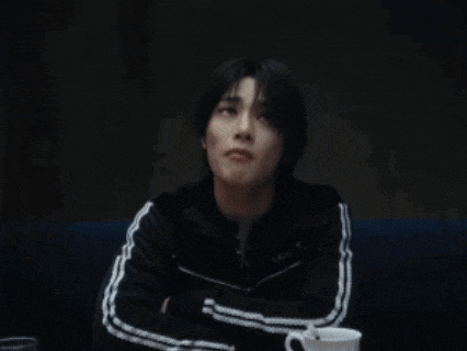 a young man in a black jacket with white stripes on the sleeves is sitting on a blue couch .