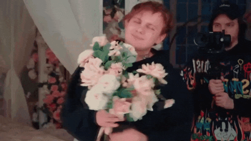 a man is holding a bouquet of flowers in front of a camera while another man takes a picture of him .