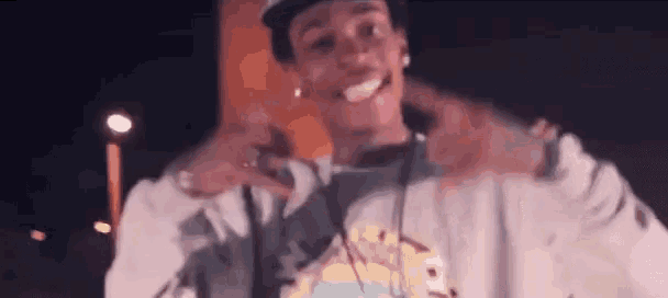 a young man wearing a hat and a sweatshirt is making a peace sign with his hands .