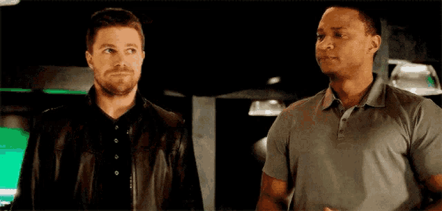 two men are standing next to each other and looking at each other in a dark room .