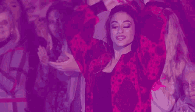 a woman is dancing in front of a crowd of people in a purple background .