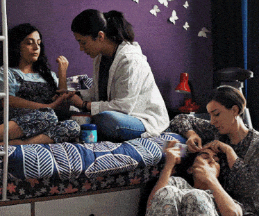 three women are sitting on a bed with a bottle of baby wipes in the background