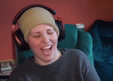 a woman wearing headphones and a beanie is laughing with her eyes closed
