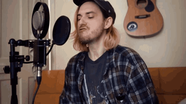a man singing into a microphone with a guitar behind him