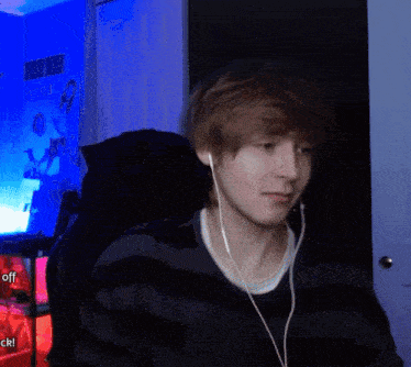 a young man wearing ear buds is sitting in front of a blue wall with a picture of a woman on it
