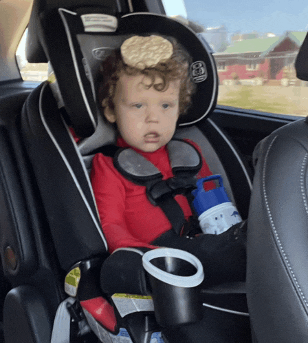 a child is sitting in a car seat with a cracker on top of his head