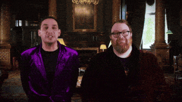 a man in a purple jacket giving a thumbs up next to another man in glasses