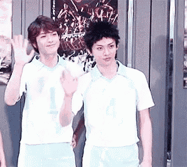 two young men are standing next to each other in front of a wall .