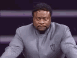 a man in a gray suit is sitting on a stage with his eyes closed and his hands folded .