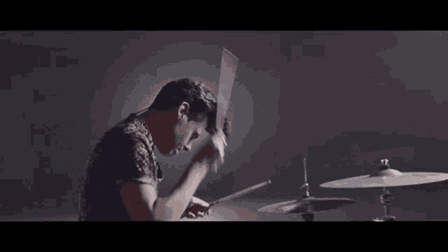 a man is playing drums in a dark room with a drum set .