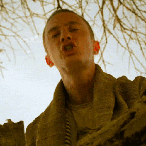 a man wearing a sweater and a striped necklace looks up at the camera