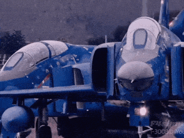 two blue fighter jets are parked next to each other in front of a sign that says t-300bo you