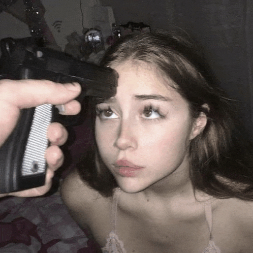 a person is pointing a gun at a young girl 's forehead .