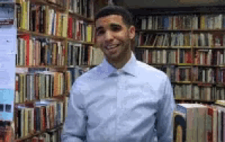 a man in a blue shirt is smiling in front of a bookshelf in a library