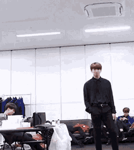 a man in a black shirt is standing in a room with people sitting on couch .