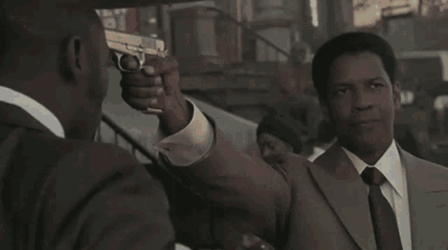 a man in a suit holds a gun in front of a barber shop