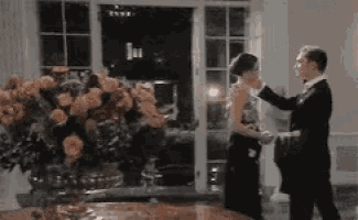 a man in a tuxedo and a woman in a dress are dancing in a room .