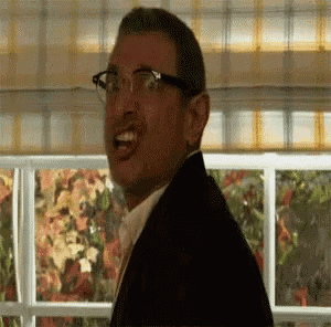 a man wearing glasses and a suit is standing in front of a window and making a funny face .