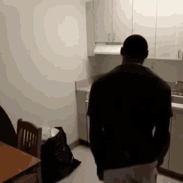 a man in a black shirt stands in a kitchen with white cabinets