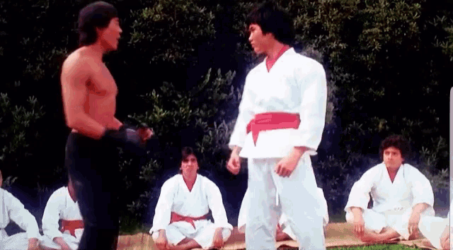 a group of men in karate uniforms are standing around a man in a white karate uniform .