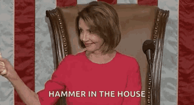a woman in a red shirt is sitting in a chair with a microphone and a hammer in the house .
