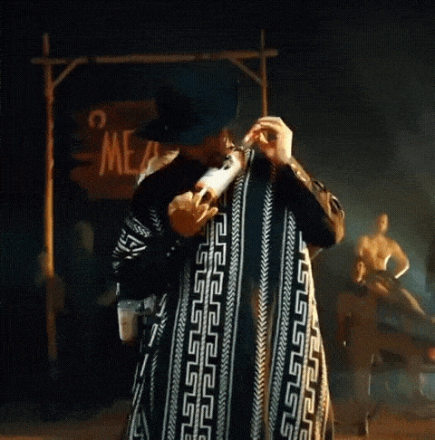 a man wearing a cowboy hat and a poncho holds a bottle of mezcal